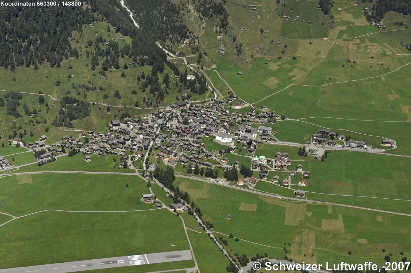 Münster (VS); (Position 2'663'408.59, 1'148'767.27). Das Dorf liegt auf der rechten Rhoneseite im oberen Goms auf rund 1350 Metern Höhe. Seit 2017 gehört Münster zur sgn. Munizipalgemeinde Goms im Bezirk Goms. Der Hauptort des Goms zählte 2016 441 Einwohner und Einwohnerinnen. - Im Vordergrund des Bildes liegt der ehemalige Militärflugplatz, der heute von der' Flugplatzgenossenschaft Münster' als Segelflugplatz genutzt wird.